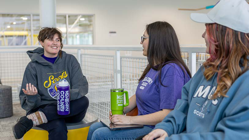 MCC students wearing MCC Scots apparel are sitting in the Foglia CATI building, each holding a colorful MCC water bottle while talking near a railing.