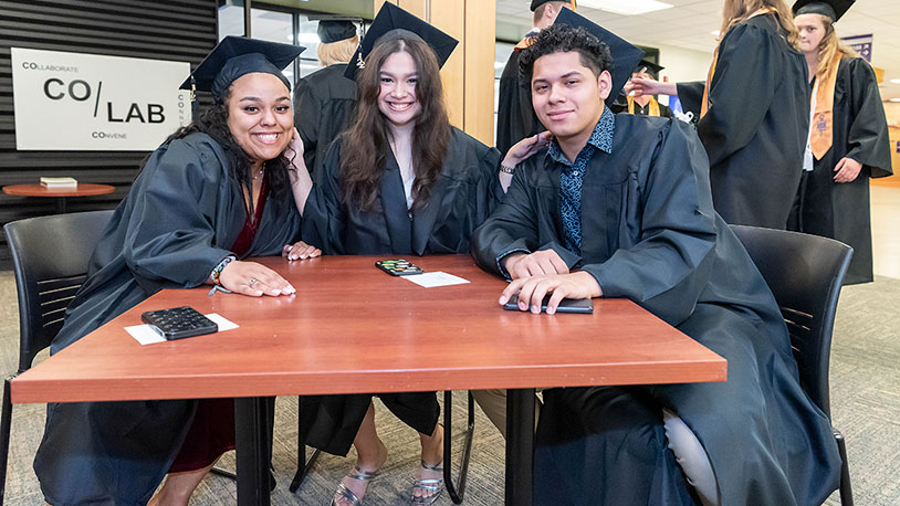Three smiling MCC graduates sit at a table after the Commencement Ceremony.
