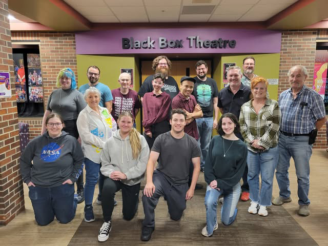The cast and crew of Arsenic and Old Lace stands in front the theatre in three rows