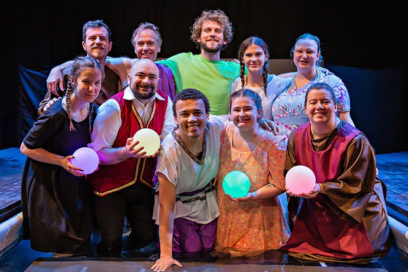 Eight members of the Metamorphoses cast stand side by side in a body of water.
