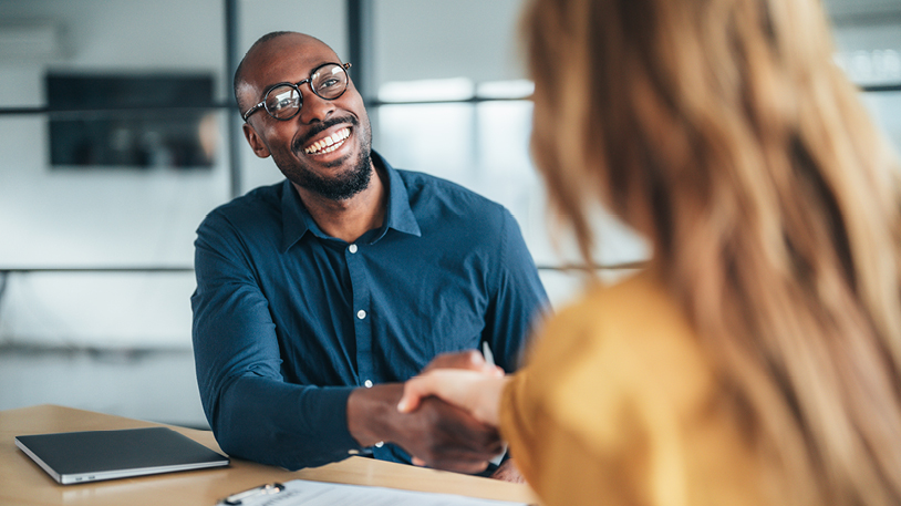 A smiling professional man shaking hands with a colleague in an office setting.