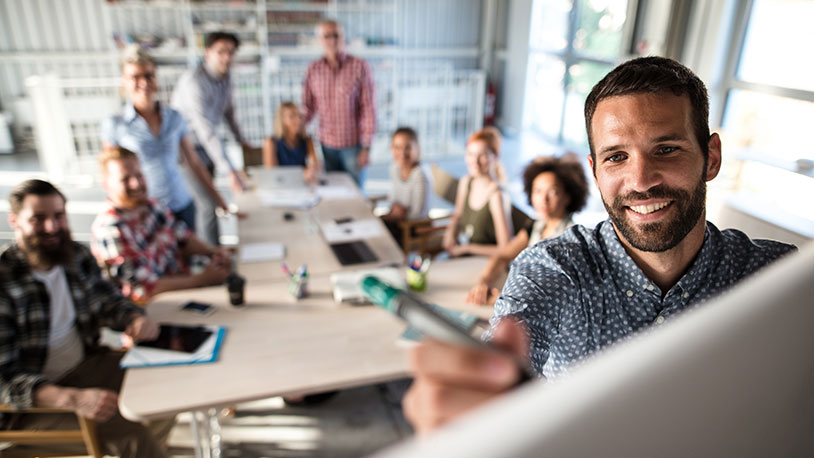 A group of people in a conference room smiling at a man writing on a white board